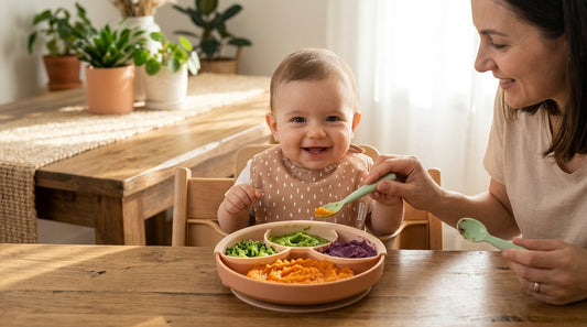 Bebelus care mananca dintr-un set de diversificare Miniware, cu piureuri colorate, supravegheat de parinte